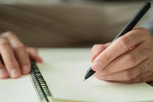 A man is writing in a notebook with a black pen photo