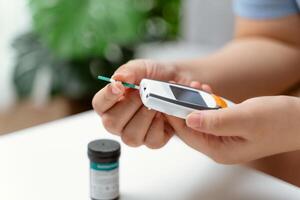 asiático mujer utilizando lanceta en dedo para comprobación sangre azúcar nivel por glucosa metro, diabetes. foto