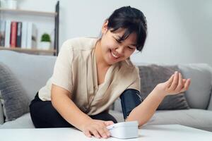 A woman is sitting on a couch and using a blood pressure monitor photo