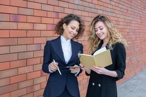 Two successful business women are talking in the city in front of a modern building. Business meeting on the street. 2 female managers with top positions. photo