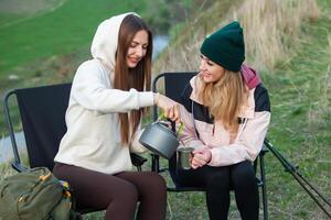 Two beautiful girls sitting in a folding chair and drinking tea in nature. Travel, traveler. photo