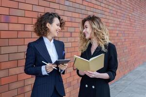 Two successful business women are talking in the city in front of a modern building. Business meeting on the street. 2 female managers with top positions. photo