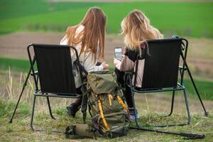 Two young women friends hikers with backpacks and trekking poles on top of a mountain. Travel, traveler. photo