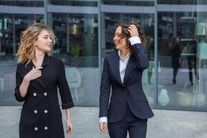 Two successful business women are talking in the city in front of a modern building. Business meeting on the street. 2 female managers with top positions. photo