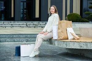 White European lady comes out of the shopping center with full bags. Beautiful woman holding shopping bags. photo