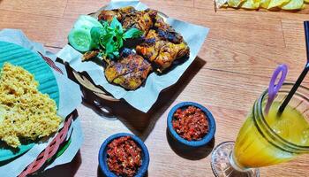 Ayam Bakar kecap manis, grilled chicken with herbs and spices from Indonesia. served with sambal, cucumber and basil leaves. photo