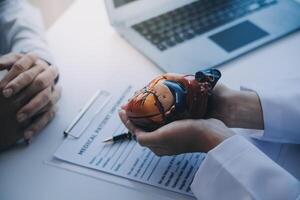 Doctor explaining heart to elderly patient. Doctor explaining the heart model. Doctors pen point to a model of the heart photo