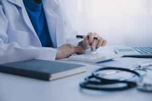 Doctor and patient sitting at the desk in clinic office. The focus is on female physician's hands filling up the medication history record form, close up. Medicine concept photo