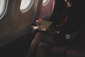 Blonde female tourist checking incoming notification on smartphone sitting on seat of airplane with netbook.Young businesswoman share media from telephone on laptop computer during plane flight photo