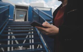 joven asiático mujer en internacional aeropuerto, utilizando móvil teléfono inteligente y comprobación vuelo a el vuelo información tablero foto