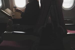 Blonde female tourist checking incoming notification on smartphone sitting on seat of airplane with netbook.Young businesswoman share media from telephone on laptop computer during plane flight photo