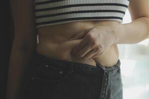 Women body fat belly. Obese woman hand holding excessive belly fat. diet lifestyle concept to reduce belly and shape up healthy stomach muscle. photo