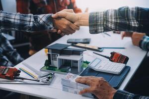 arquitecto y ingeniero construcción trabajadores sacudida manos mientras trabajando para trabajo en equipo y cooperación concepto después terminar un acuerdo en el oficina construcción sitio, éxito colaboración concepto foto