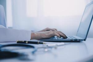 Doctor and patient sitting at the desk in clinic office. The focus is on female physician's hands filling up the medication history record form, close up. Medicine concept photo