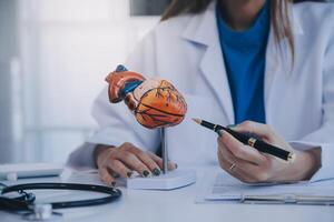 Doctor explaining heart to elderly patient. Doctor explaining the heart model. Doctors pen point to a model of the heart photo
