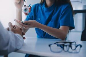 Close-up of Asian female doctor talking with elderly patient showing eyeball model and explaining eye disease in hospital photo