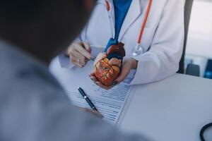 Doctor explaining heart to elderly patient. Doctor explaining the heart model. Doctors pen point to a model of the heart photo