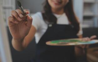 Cropped image of female artist standing in front of an easel and dipping brush into color palette photo