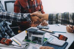 arquitecto y ingeniero construcción trabajadores sacudida manos mientras trabajando para trabajo en equipo y cooperación concepto después terminar un acuerdo en el oficina construcción sitio, éxito colaboración concepto foto