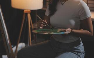 Cropped image of female artist standing in front of an easel and dipping brush into color palette photo