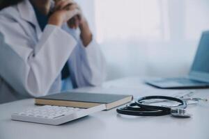 médico y paciente sentado a el escritorio en clínica oficina. el atención es en hembra médico manos relleno arriba el medicación historia grabar forma, cerca arriba. medicina concepto foto