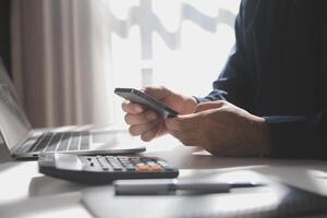 Side view shot of a man's hands using smart phone in interior, rear view of business man hands busy using cell phone at office desk, young male student typing on phone sitting at wooden table, flare photo