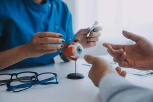 Close-up of Asian female doctor talking with elderly patient showing eyeball model and explaining eye disease in hospital photo