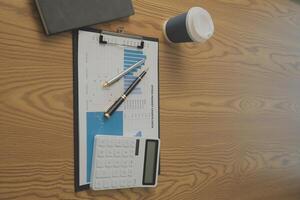 Close up view of simple workspace with laptop, notebooks, coffee cup and tree pot on white table with blurred office room background photo