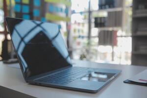 cerca arriba ver de sencillo espacio de trabajo con computadora portátil, cuadernos, café taza y árbol maceta en blanco mesa con borroso oficina habitación antecedentes foto