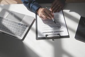 Asian businessman reviewing document reports at office workplace with computer laptop. legal expert, professional lawyer reading and checking financial documents or insurance contract photo