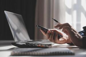 Side view shot of a man's hands using smart phone in interior, rear view of business man hands busy using cell phone at office desk, young male student typing on phone sitting at wooden table, flare photo