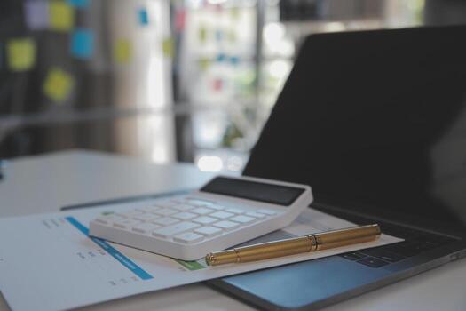 Close up view of simple workspace with laptop, notebooks, coffee cup and tree pot on white table with blurred office room background photo
