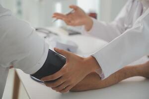 Male doctor uses a blood pressure monitor to check the body pressure and pulse of the patients who come to the hospital for check-ups, Medical treatment and health care concept. photo