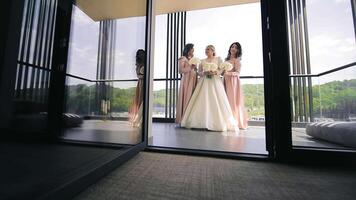 novia con damas de honor posando por ventana, un sonriente novia y damas de honor en elegante vestidos por un grande ventana. video