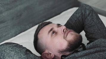 Pensive Man Lying on Bed, Overhead view of a young man lying on a bed, looking contemplative. video