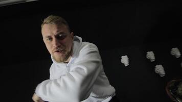 Dynamic Rapper Gesturing in Studio, A man in a white hoodie gestures energetically in a dark studio, flanked by sculptures. video