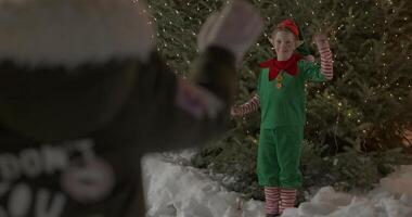 garçon habillé comme Noël elfe agitant main permanent dans de face de Noël arbre video