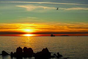 Sunset over the ocean with island and ship in silhouette photo