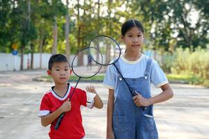 An Asian girl and boy stand together holding badminton rackets and white shuttlecocks. photo