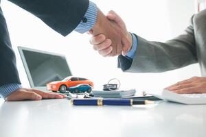 customer and car dealer shake hands after agreeing to sales contract before making contract payment and handing over car keys to customer. concept of handshake between customers and car dealers. photo