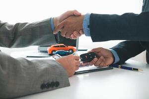 customer and car dealer shake hands after agreeing to sales contract before making contract payment and handing over car keys to customer. concept of handshake between customers and car dealers. photo