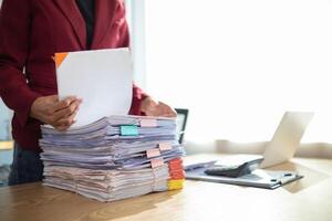 secretary is searching through pile of important documents on office table deliver them to manager for presentation in time at meeting. Concept of difficulty finding information from piles of document photo