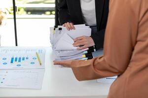 A young secretary receives a pile of documents to find important information for the company manager to use in a meeting. The concept of finding important documents from piles of overlapping documents photo