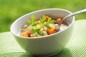 Vegetable soup with bean and carrots on green background photo