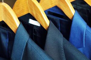 Row of men's suits hanging on rack for sale photo