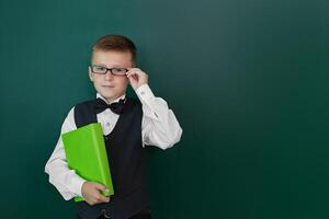 contento linda inteligente chico con un arco Corbata y en lentes con libro en su mano. primero hora a escuela. espalda a escuela. foto