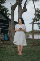 Portrait of a pretty young woman dressed in white dress holding rose flowers photo