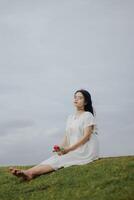 retrato de un bonito joven mujer vestido en blanco vestir participación Rosa flores foto