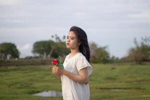 retrato de un bonito joven mujer vestido en blanco vestir participación Rosa flores foto