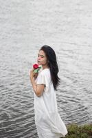 retrato de un bonito joven mujer vestido en blanco vestir participación Rosa flores foto